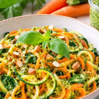 Warmer Zucchini-Möhren-Nudelsalat mit Spinat und cremigem Mandel-Kräuter-Pesto in einer Schale Nahaufnahme