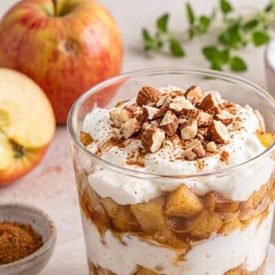 Basisches Apfel-Zimt-Kokos-Dessert mit warmen Apfelstücken, Kokosjoghurt und gehackten Mandeln im Glas Nahaufnahme